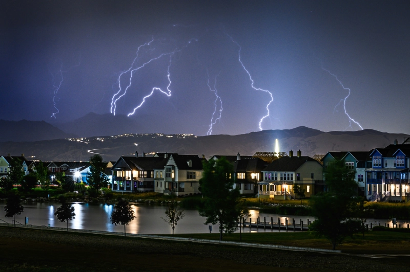 A view of houses and buildings with lightning in the background.